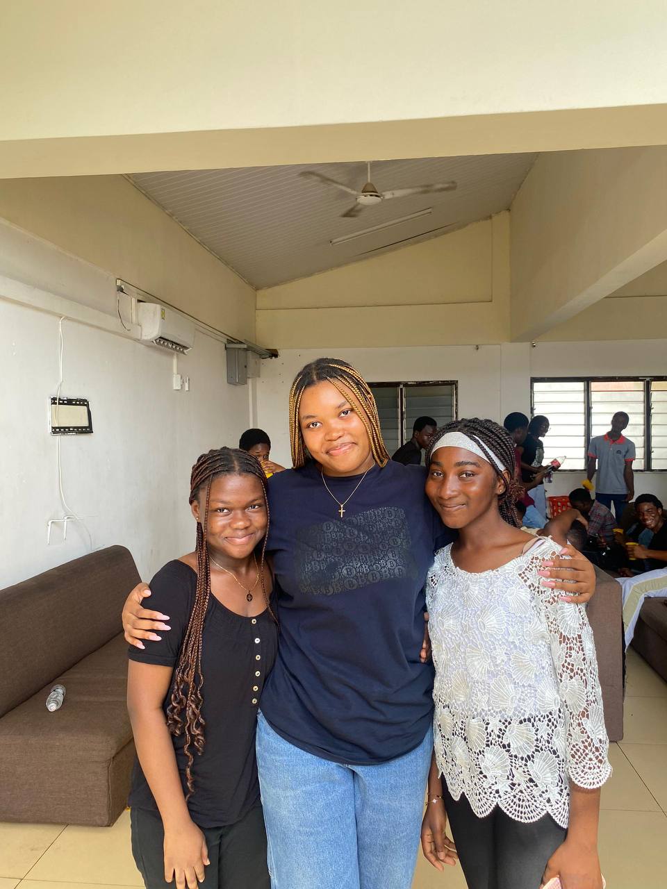 Two people pose joyfully in front of a pink backdrop, one pushing the other on a skateboard, celebrating Kings & Priests kinship.
